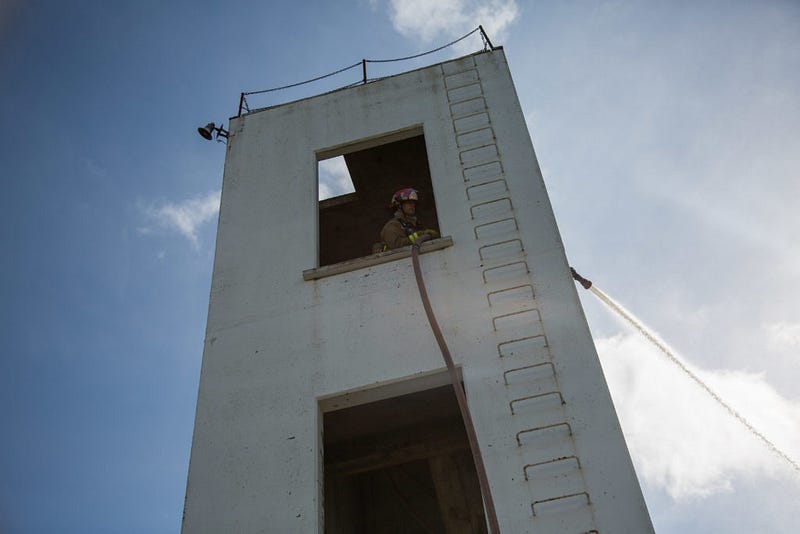 A the top of a three-story tower at the Bellingham Fire Department training grounds, McDonald and Dowdy use a fire hose to spray 300 gallons of water per minute over the parking lot below. Firefighters will often use a “hotel pack,” a shorter hose that can is folded up and can be connected to pipes in stairwells of hotels or apartment buildings, instead of dragging a long hose connected to the fire truck up a high-rise building.