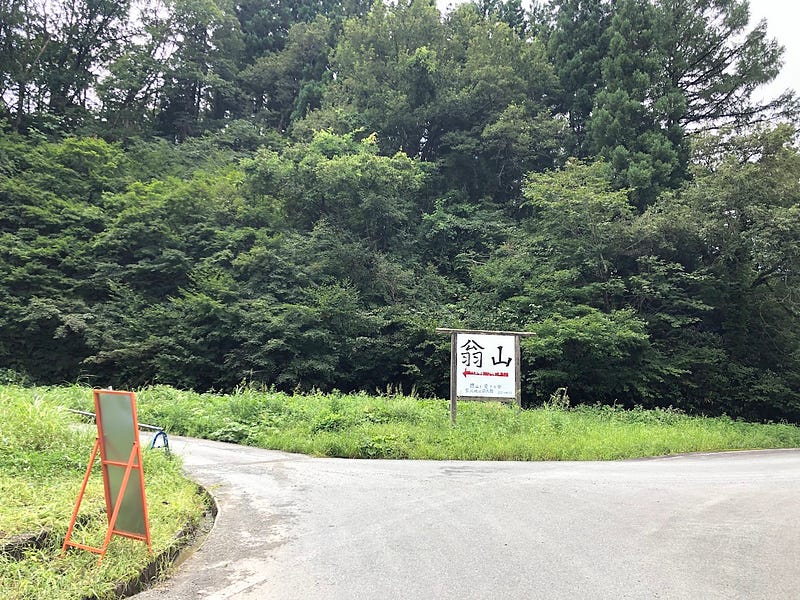 A sign on a road pointing to the Okina-san trailhead