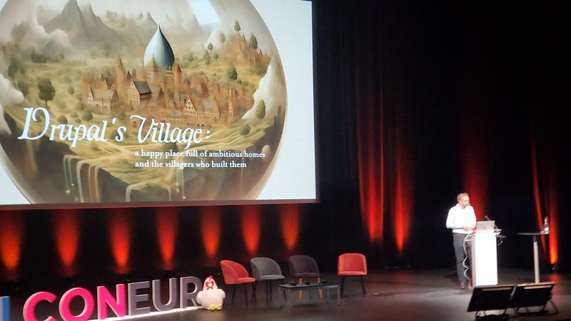 Dries presenting his Driesnote (keynote) — Slide is of a stylized Drupal Village.