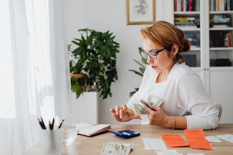 A woman sitting at a desk with money in one hand and calculating
