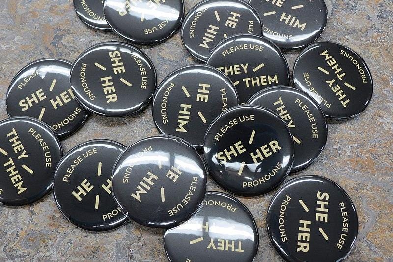 A cluster of pronoun buttons that read, “Please Use She/Her, He/Him, or They/Them Pronouns”