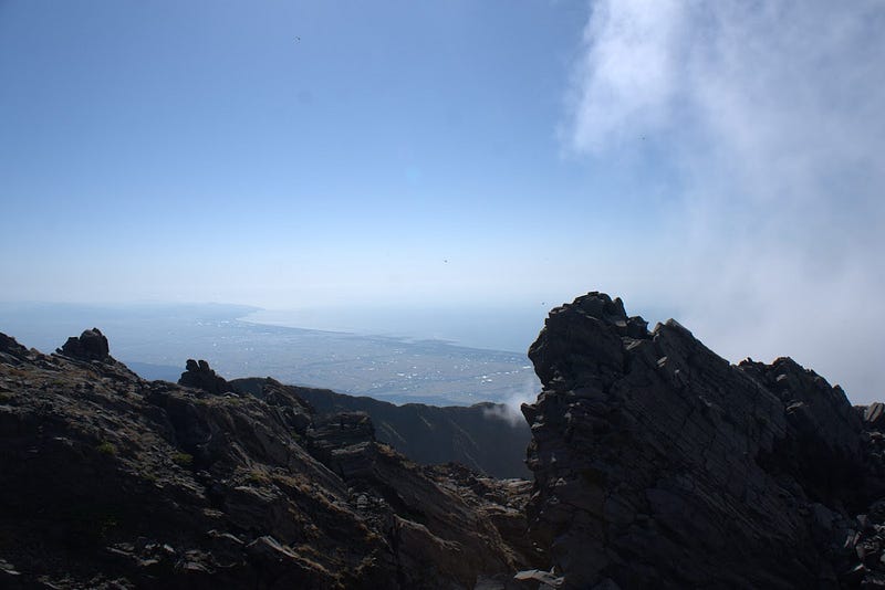 The rocky landscape of the summit of Chokai-san (Mt. Chokai) in the foreground, with the distant Sakata City and Sea of Japan.