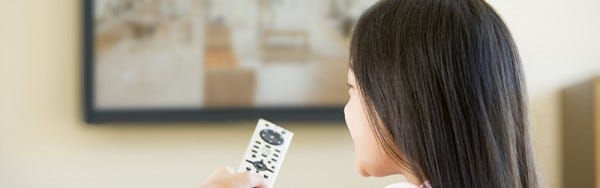 Young girl in living room with flat screen television and remote control sitting on sofa watching TV