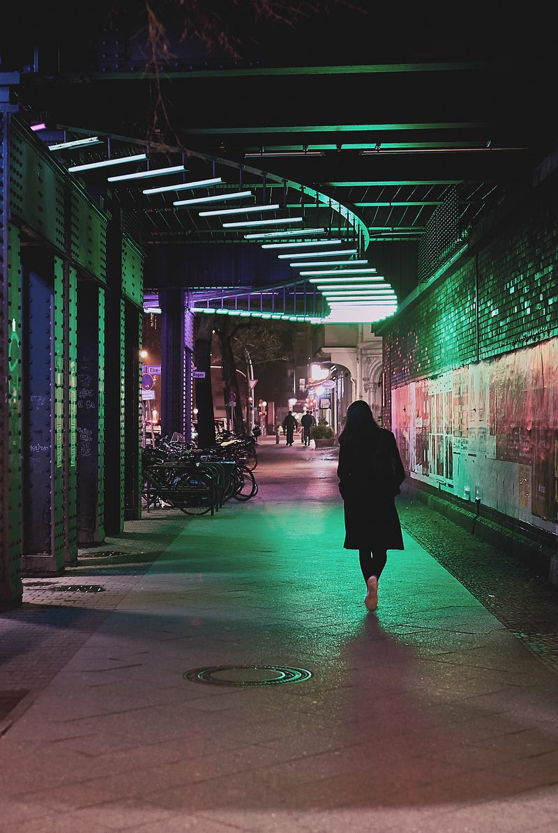 A woman walks down a city sidewalk at night.