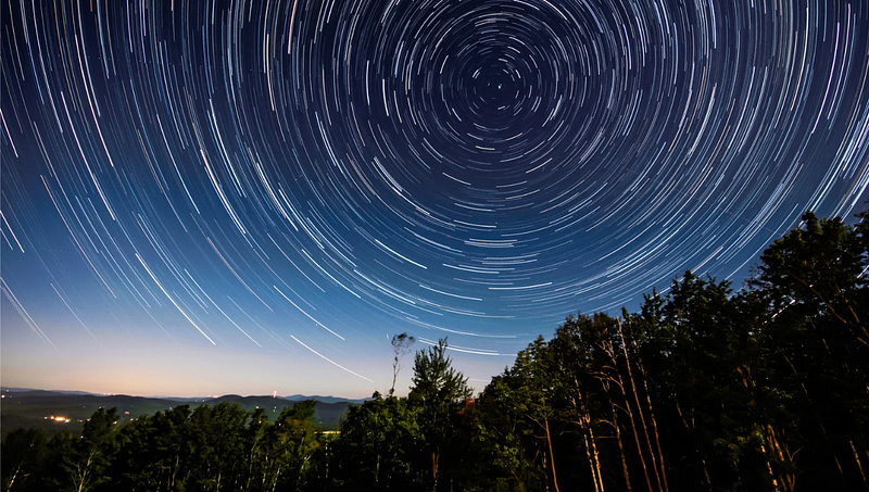 Star trails in the night sky — A long-exposure photograph capturing circular star trails in the night sky above a forested landscape.