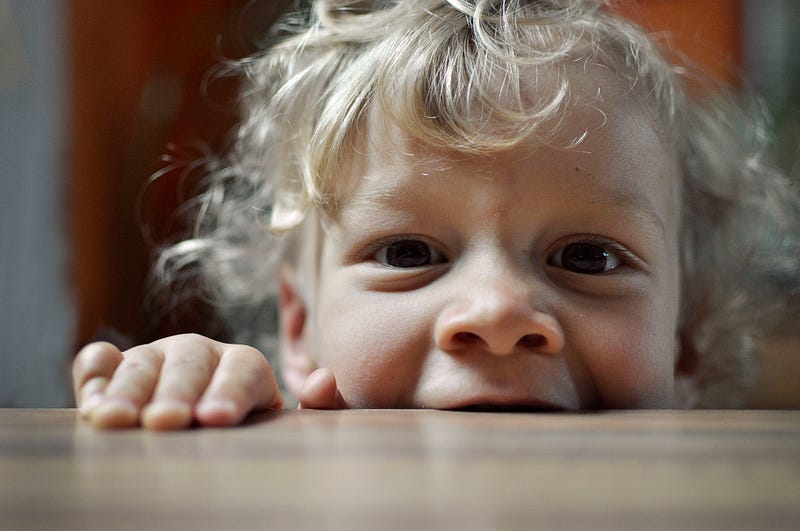 Child peering over table into camera.