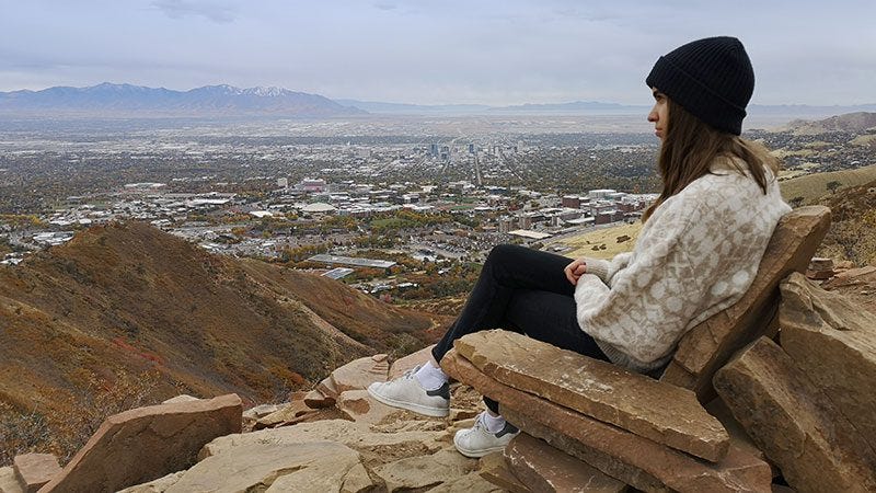 Una mujer se sienta en una formación rocosa similar a un asiento en la parte superior de la caminata Living Room Hike en Salt Lake City. 
