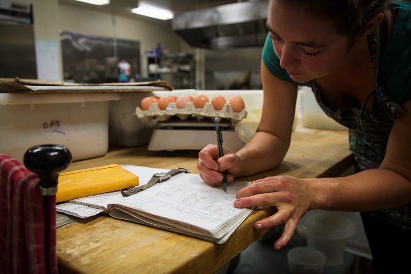 Sophie Williams takes notes on her baking times and ingredients in between batches. She used to use her laptop to document her notes but switched back to pen and paper to prevent her laptop from getting dirty, she says.