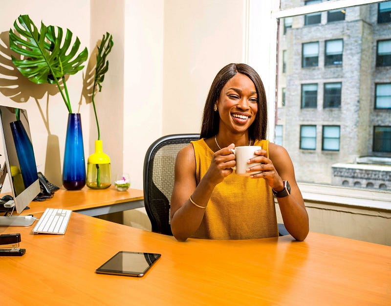 a person sitting on their desk while holding a white mug and smiling