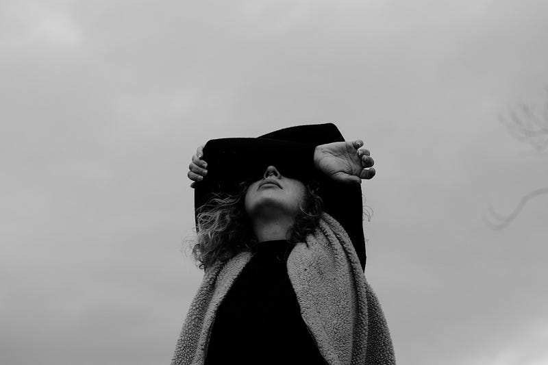 Black and white image of a woman with her arms crossed over the top of her face.