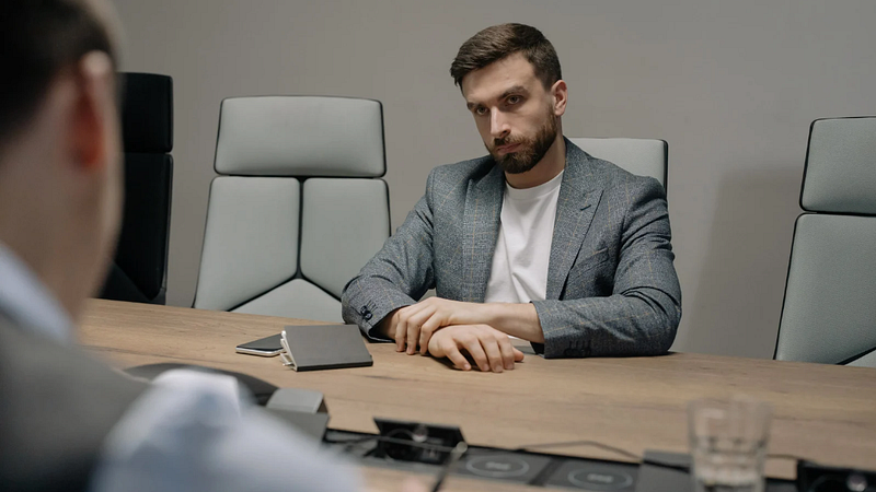 A man sits on the far side of the table looking at his boss.