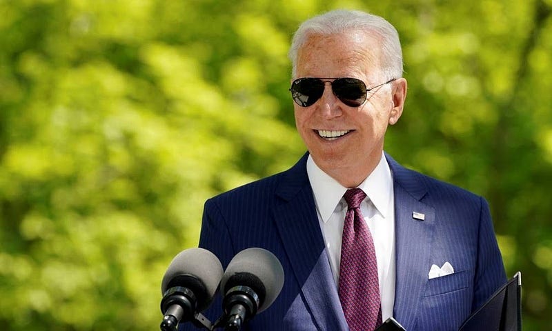 Joe Biden de óculos escuro e sorrindo após ter cumprido sua promessa em seus primeiros 100 dias