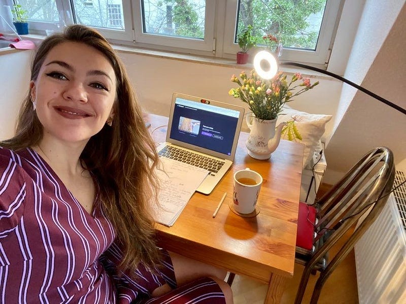 Young woman (Anastasia) taking a selfie sitting on a table with her laptop, mug and flowers