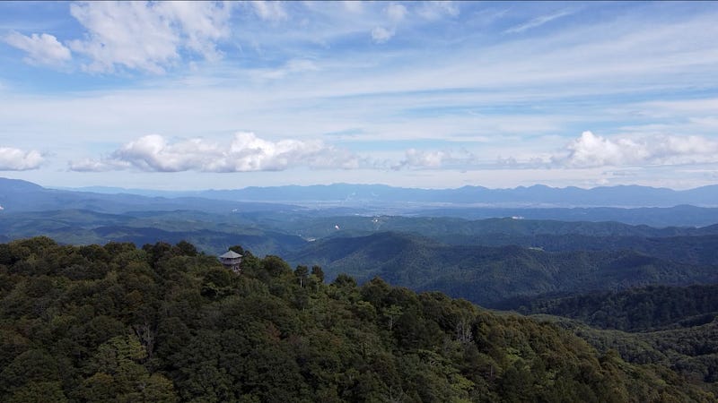 A tower sticks out of the deep green forests at the summit of Daizumori-yama with inland Yamagata Prefecture far off in the distance.