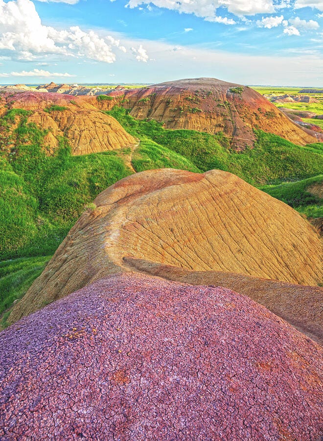 A vivid spring landscape of Badlands National Park with sharp ridges, grassy meadows, and dramatic skies, photographed by Dan Sproul.
