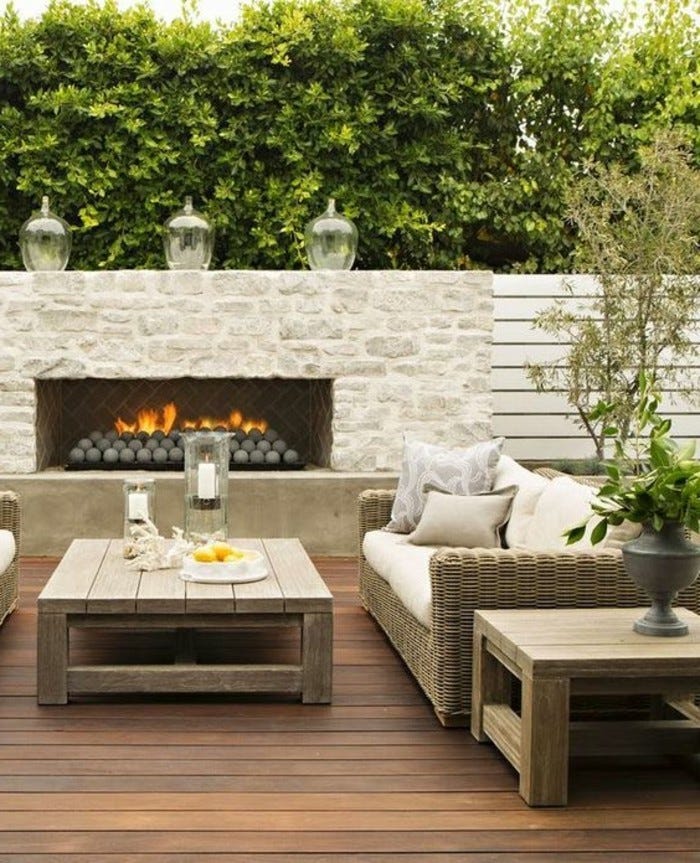 moderne-gartengestaltung-mit-sichtschutz-kamin-rattan-loungemöbeln-und-couchtisch-aus-holz