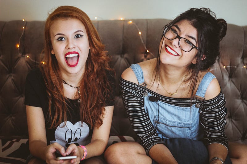 Two young teenage girls on a cell phone smiling and laughing.