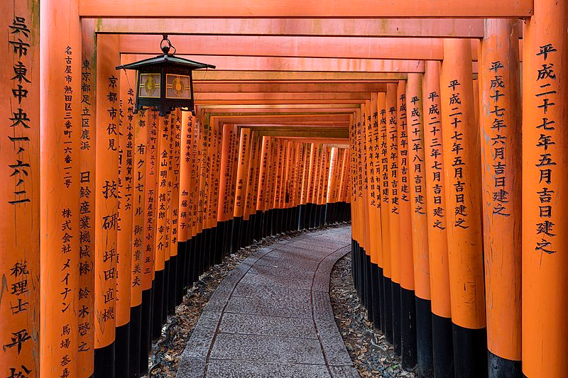 A photograph of a path lined with torii and with a lantern at Fushimi Inari Taisha shrine in Kyoto, Japan