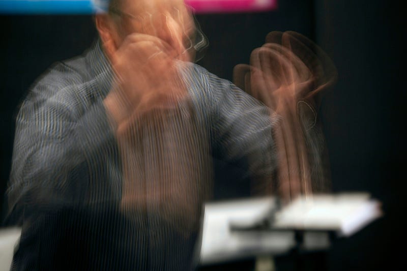 A conductor is blurred as they move to guide an orchestra.