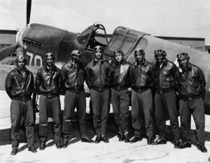 A group of pilots standing in front of a warplane.
