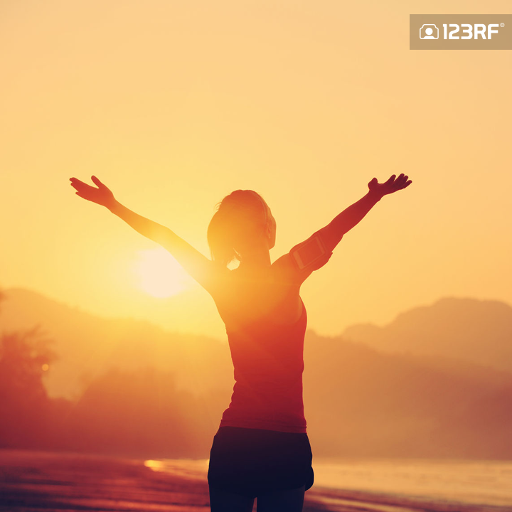 Stock Photo - strong confidence woman open arms under the sunrise at seaside