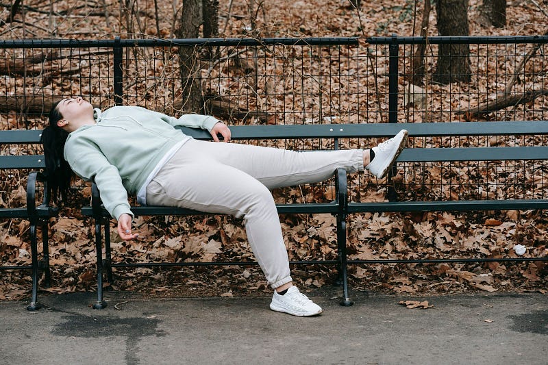 an overworked person lying on a park bench