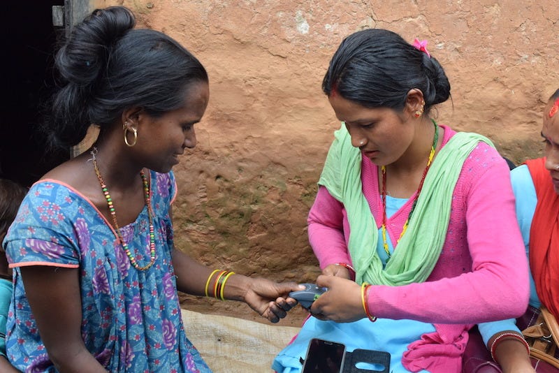 A picture of two women, one holding a fingerprint scanner, the other placing their thumb on the scanner window