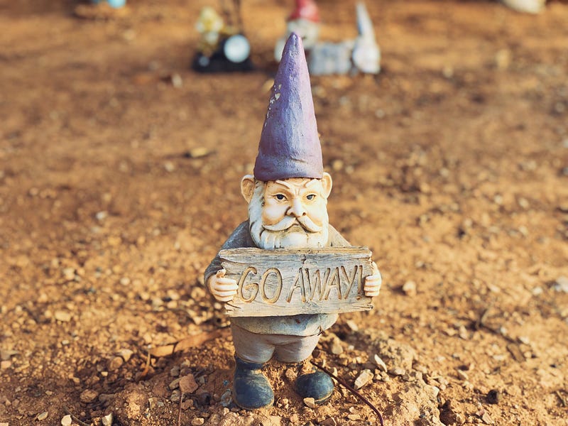 A garden gnome holding a sign that says “Go Away”