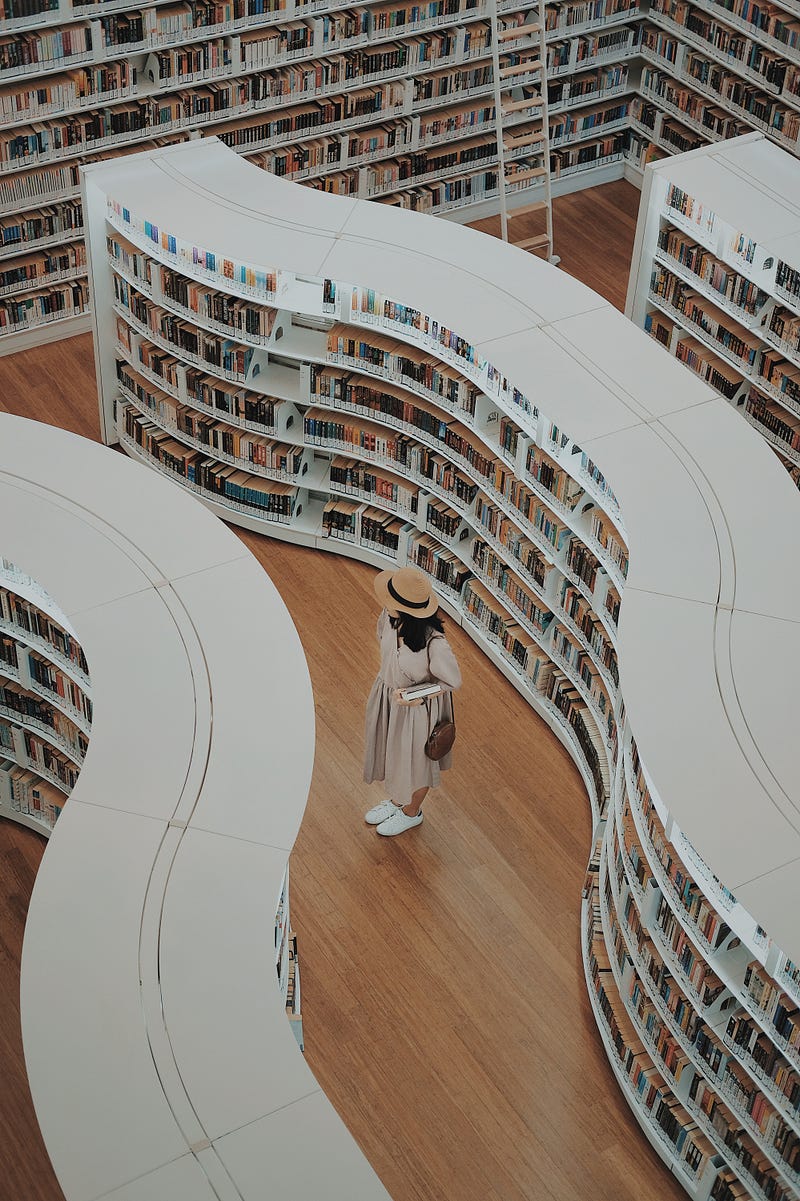Woman with white hat in library picking a book.