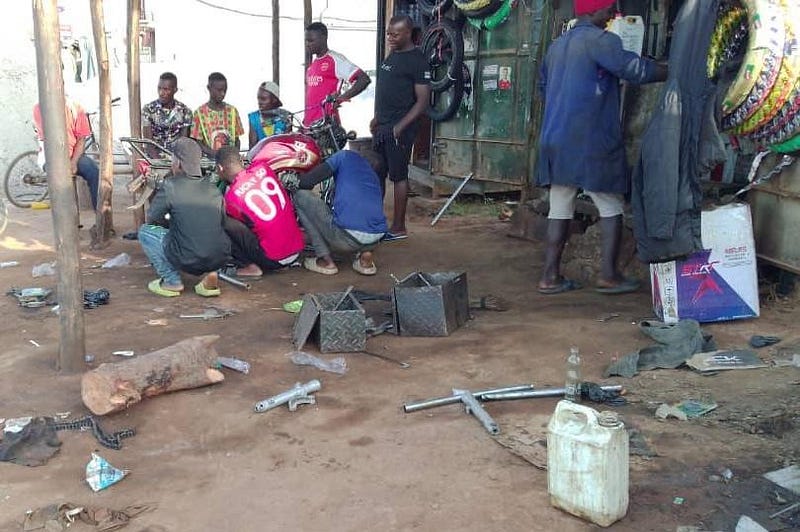 Junior mechanics and a customer looking on while a senior mechanic repairs a motorcycle at a garage in Kampala. Credit: Geofrey Ndhogezi.