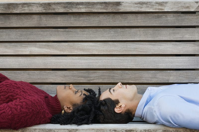 Young couple lying on bench head to head. African woman and young man looking up, lying on bench. Pensive couple lying on back and thinking about their future with copy space.