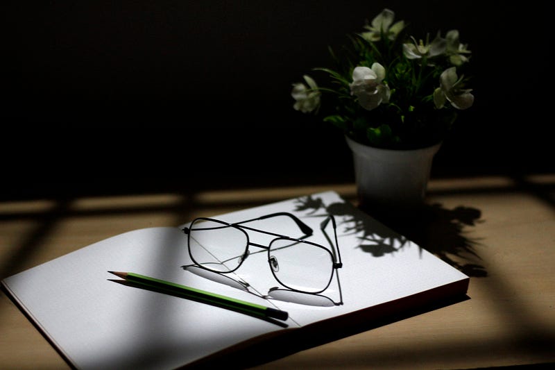 A pencil and glasses rested on top of a plain notebook