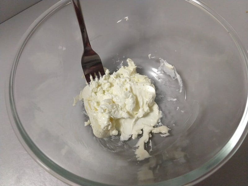 A glass bowl with a portion of cream cheese in the bottom, with a fork sticking out of it.