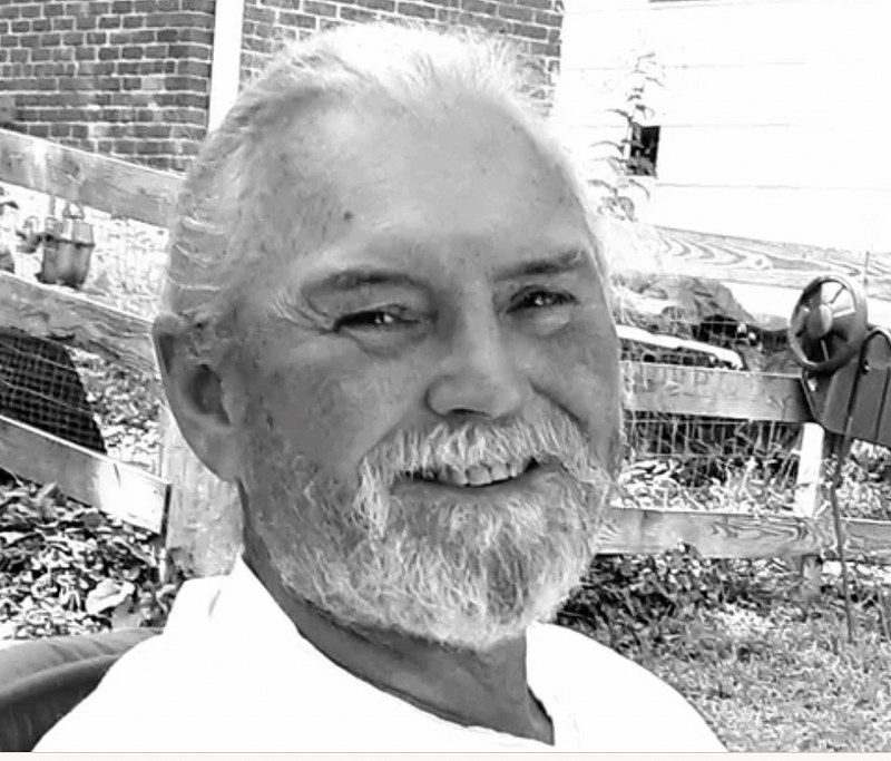 A white man with a white beard and long white hair pulled into a ponytail smiles for the camera.