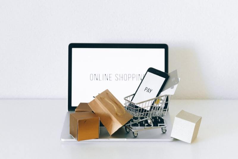 Online shopping icon. A small shopping cart on top of a laptop.