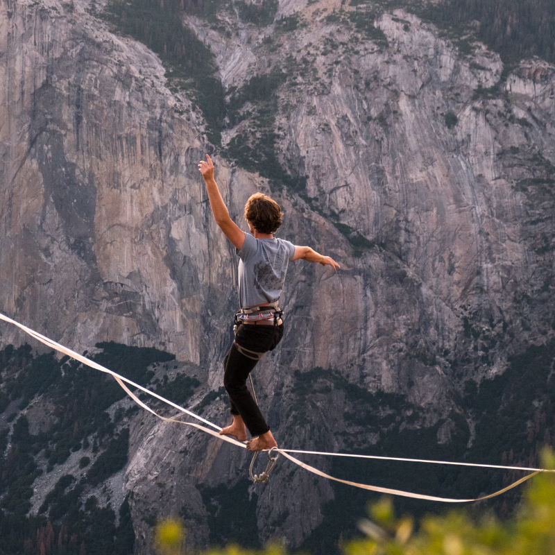 A man balancing on tight rope with mountains in the background.