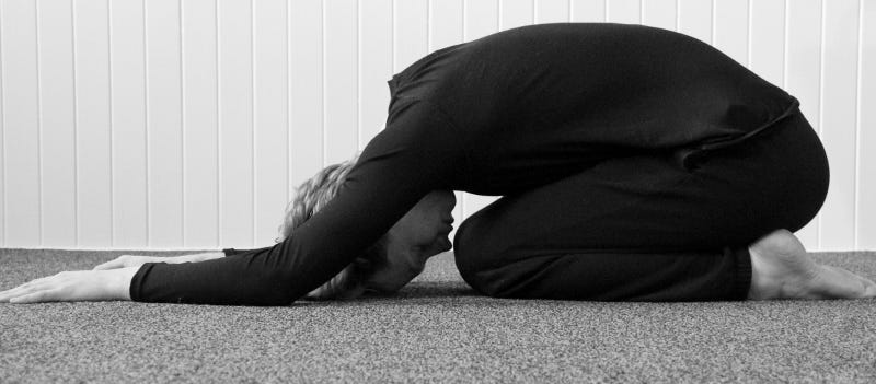 A person practicing a forward bending yoga posture while kneeling down.