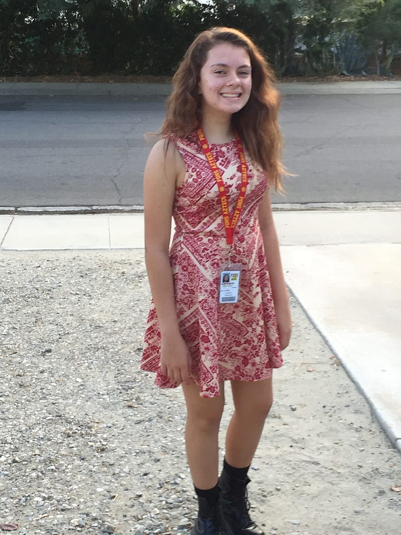 A photo of me in a red dress and combat boots, standing on gravel and smiling at the camera.