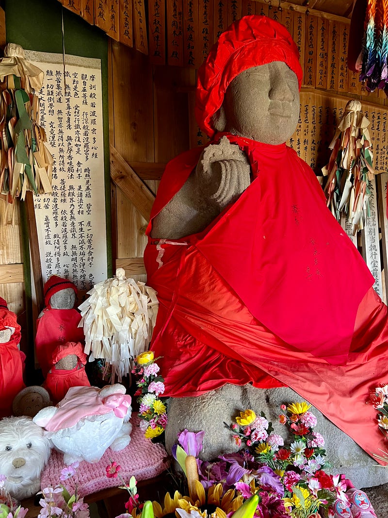 Statue with red robe and hat surrounded by flowers and toys.