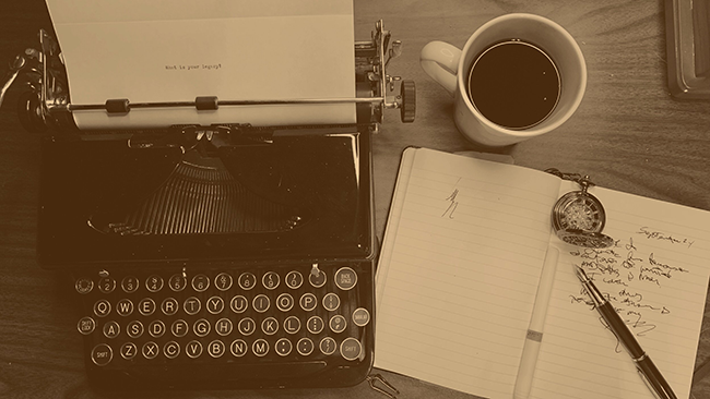 An overhead shot of a manual typewriter, cup of coffee, pocket watch and a journal with a fountain pen.