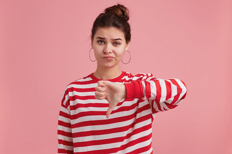 Portrait of young female with freckles, wears striped longsleeve, looking at the front with displeasure, being moody