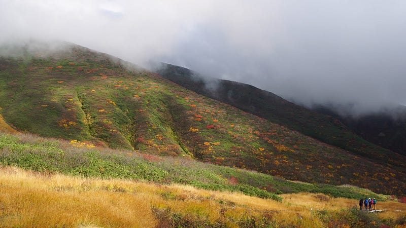 Hikers stand in awe at the awesome display of the green, yellow, and red autumn leaves Mt. Ubagatake is showing.