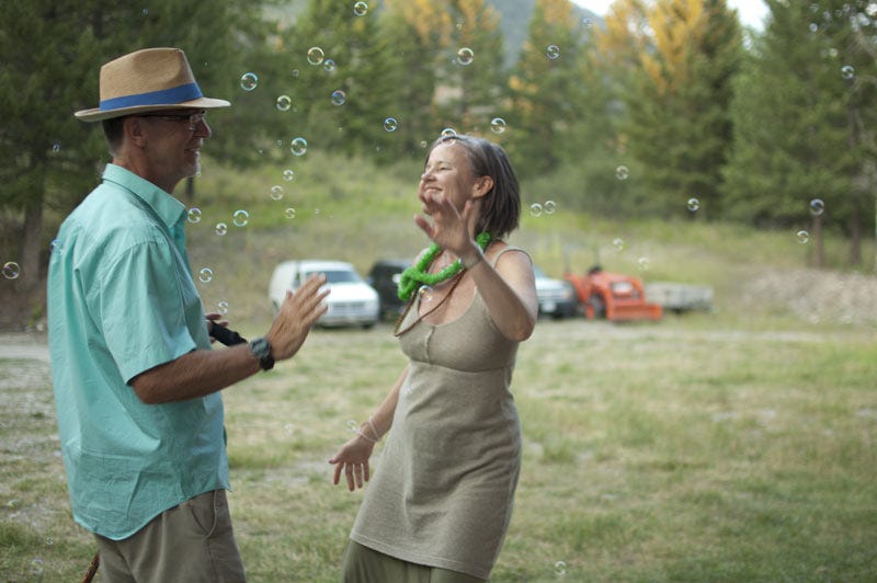 A white man and white woman standing in a field playing with bubbles