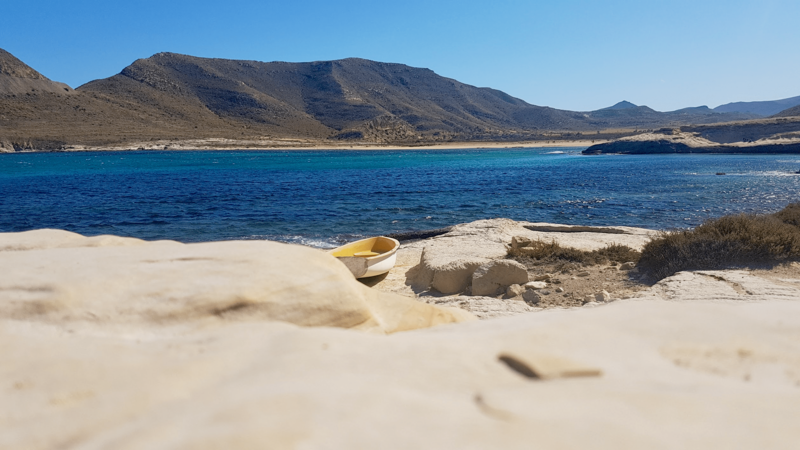 A little white and yellow boat lays on the shore, surrounded by arid mountains and a blue Mediterranean sea in Southern Spain.
