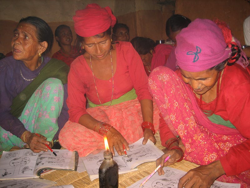 World Education Nepal Three Nepali women sit on the floor writing in notebooks, in front of a candle.