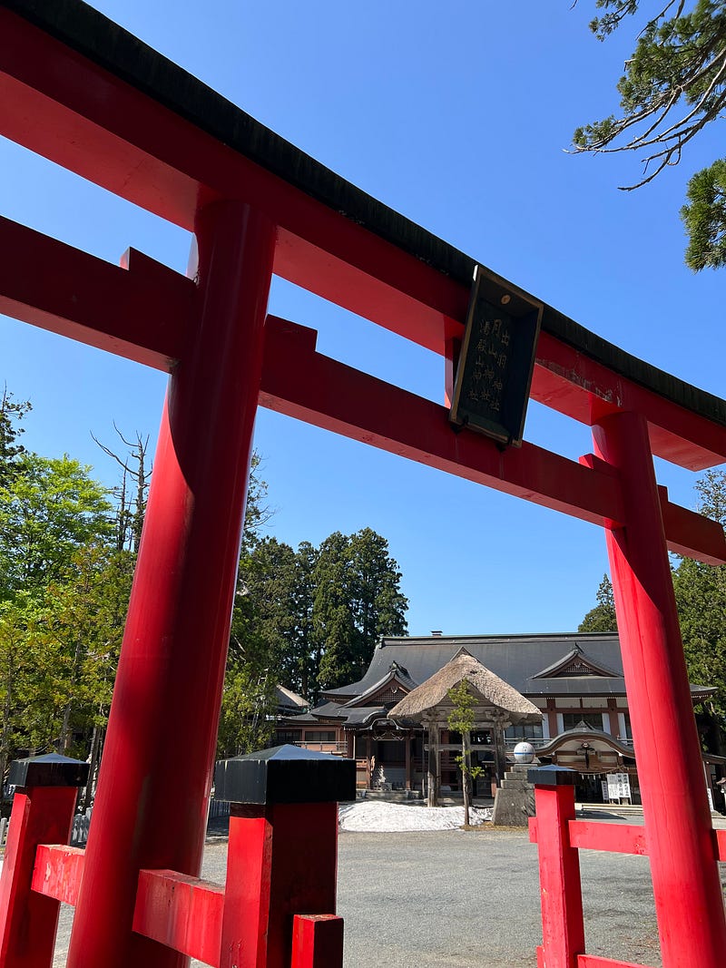 Red torii gate against blue sky fronts the Mount Haguro Shrine.