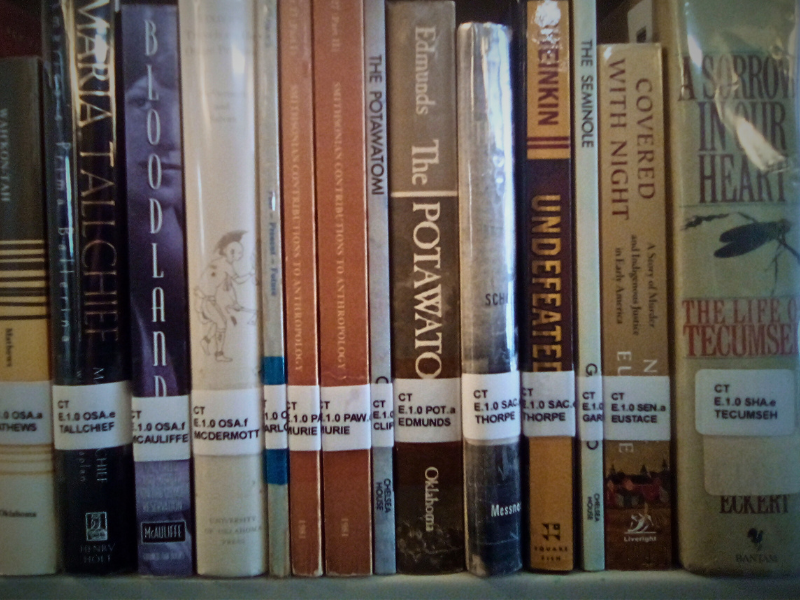 Picture showing a shelf of books in the Choska Talfa Room, spine labels facing out to show, to show the Fus Fixico Cataloging System in-action.