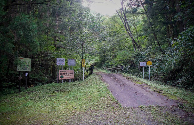 A mountain road crosses over a bridge into a deep forest with signs on either side leading to the Ennoji Trailhead of Mt. Kyogakura located in Sakata City, Yamagata Prefecture, in Tohoku, North Japan.