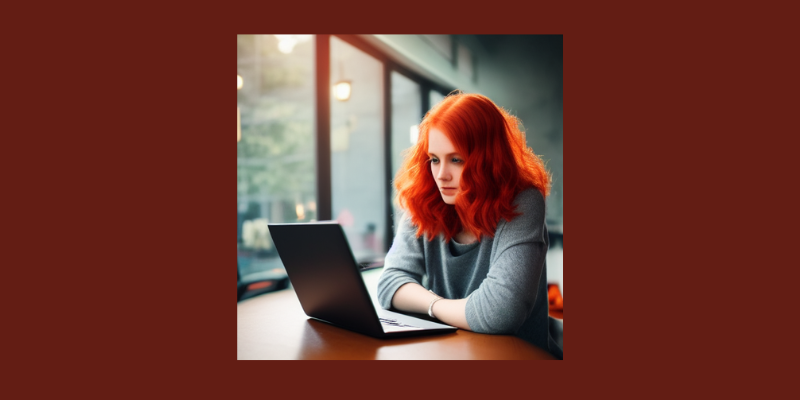 Red-haired woman working on a laptop at a cafe.
