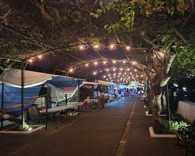 Foliage covers a lighted pathway lined with vendor booths.